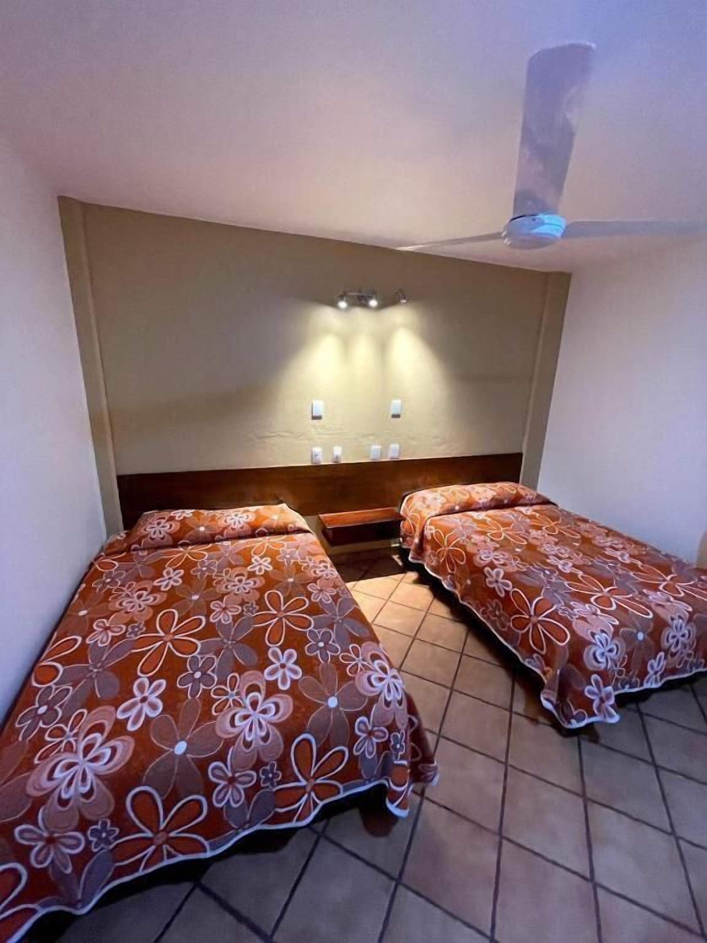 A room with two beds, a ceiling fan, and wall-mounted lights.