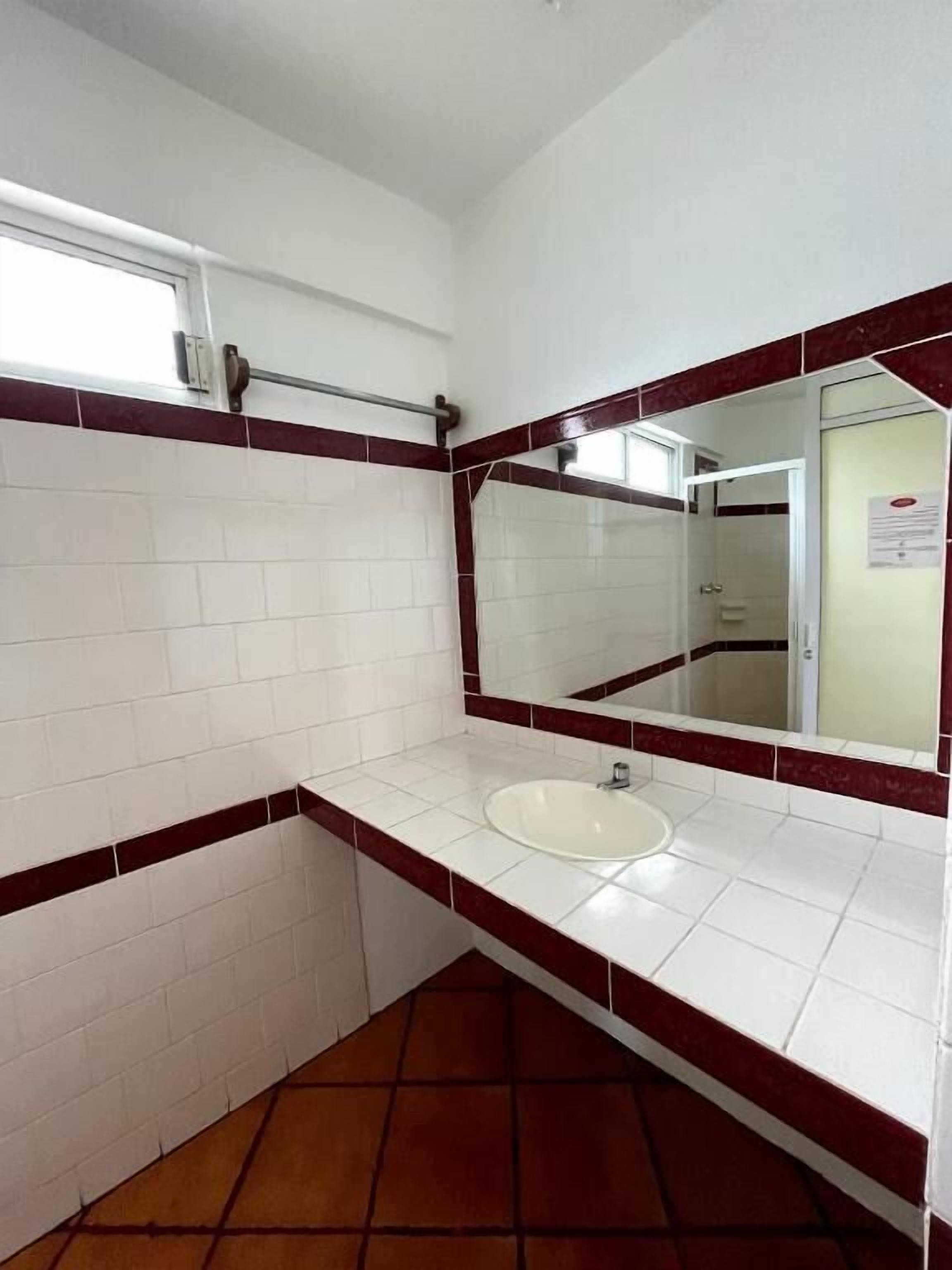 A bathroom with white tiled walls, a red-tiled floor, a white sink, and a mirror.