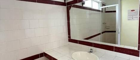 A bathroom with white tiled walls, a red-tiled floor, a white sink, and a mirror.