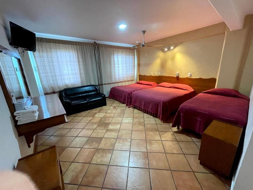 A hotel room with a bed, a desk with a flat-screen TV, a ceiling fan, and a window with curtains.
