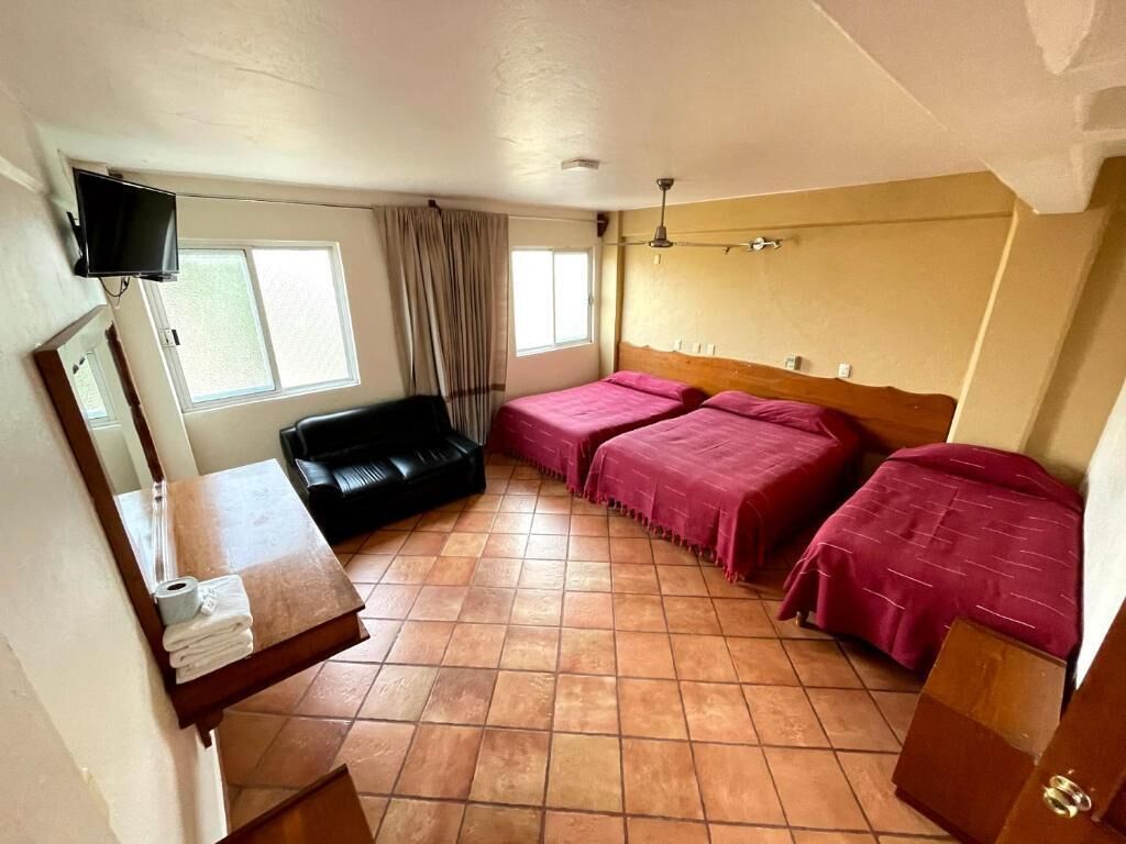 A room with two beds, a television, a sofa, a mirror, and a window.