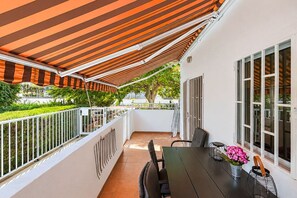 Ein überdachter Außenbereich mit Tisch und Stühlen, einem Blumentopf und Blick ins Grüne.