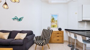 Un soggiorno moderno con un divano, una poltrona a righe, un tavolino in legno e una zona cucina con uno sgabello da bar.