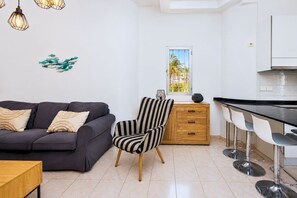 Ein modernes Wohnzimmer mit einer Couch, einem gestreiften Sessel, einem Holztisch und einer Küchenzeile mit Barhocker.