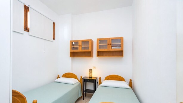 Una stanza piccola e stretta con due letti di legno, un comodino e due pensili in legno sopra i letti.