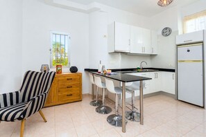 Eine moderne Küche mit weißen Schränken, einer schwarzen Arbeitsplatte und einem Edelstahl-Kühlschrank. Ein Holfach mit Schubladen und ein gestreifter Stuhl sind ebenfalls vorhanden.