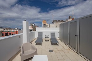 Terraço no telhado com duas cadeiras de descanso, uma mesa e um guarda-roupa.