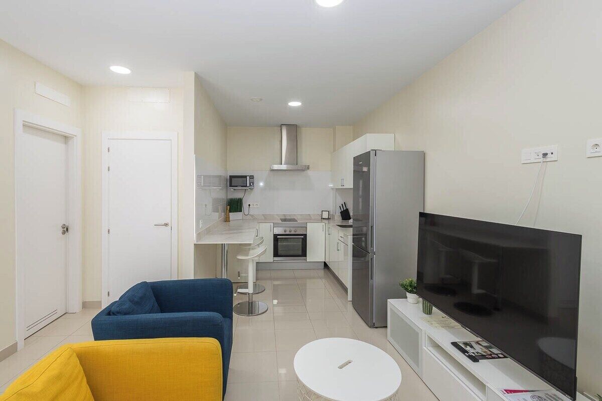 A compact living space with a kitchenette, a flat-screen TV, a sofa, and a small dining table.