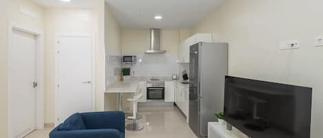 A compact living space with a kitchenette, a flat-screen TV, a sofa, and a small dining table.