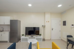 A modern living room with a flat-screen TV, a dining table, a sofa, and a kitchen area with a refrigerator. - GuestReady - 01A Livian Suites 1A Int 2pax (Las Palmas de Gran Canaria)