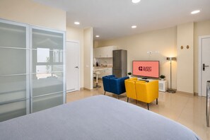 A modern hotel room with a bed, a TV displaying 'GUEST READY', a kitchenette, and a dining area with two chairs. - GuestReady - 01A Livian Suites 1A Int 2pax (Las Palmas de Gran Canaria)