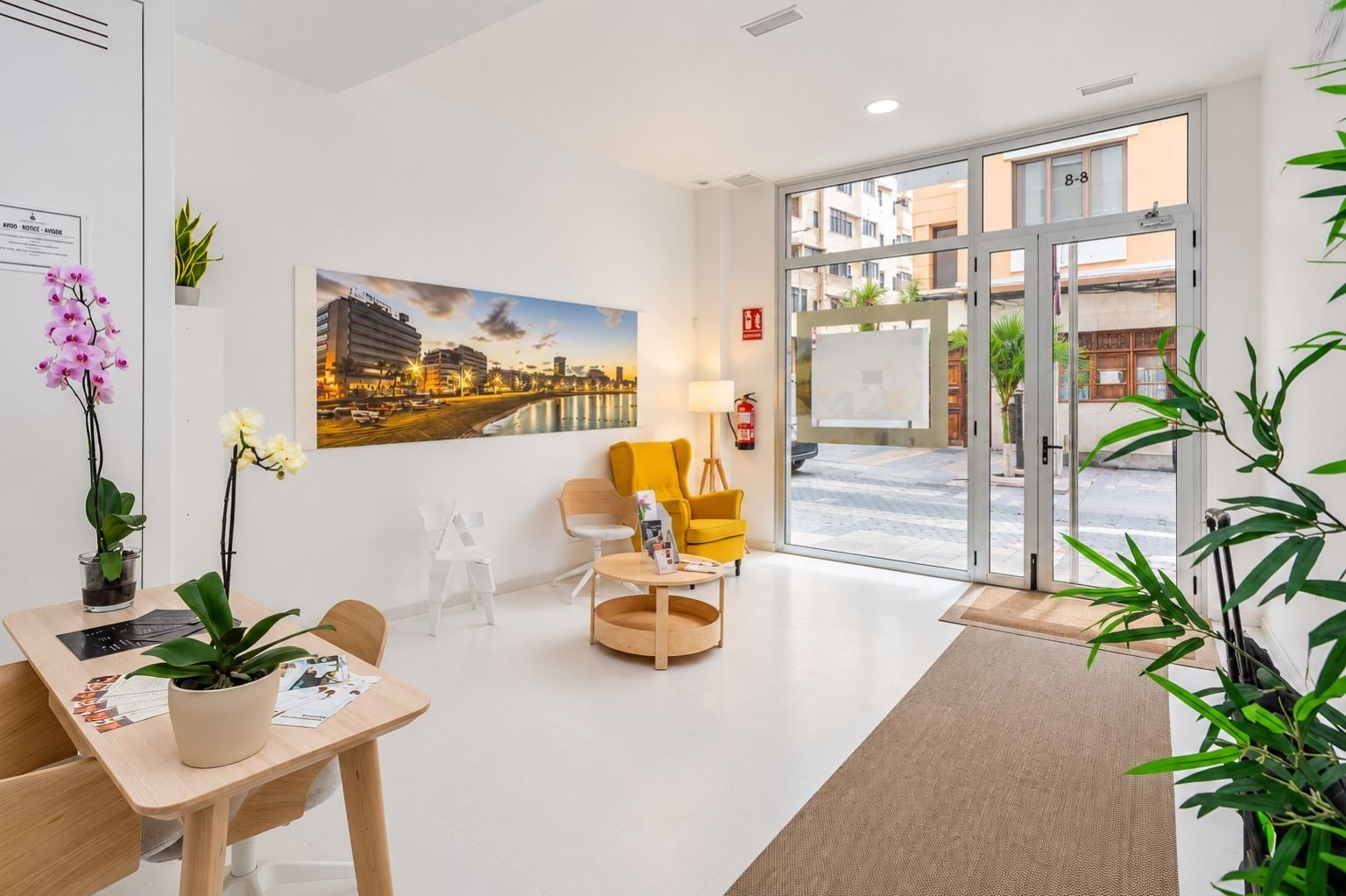 Un hall d’hôtel comprenant un comptoir d’accueil, un espace salon, un grand tableau représentant un paysage urbain et une vue à travers les portes vitrées.