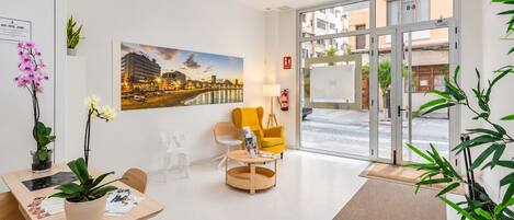 A hotel lobby with a reception desk, seating area, a large cityscape painting, and a view through the glass doors.