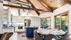 A modern kitchen with white cabinets, a blue island, and a dining area with a round table set for six. - Walk to Beech Slopes | Hot Tub, Sleeps 8 (Beech Mountain)