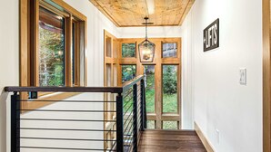 A wooden staircase with a metal railing, large windows, and a hanging light fixture. - Walk to Beech Slopes | Hot Tub, Sleeps 8 (Beech Mountain)