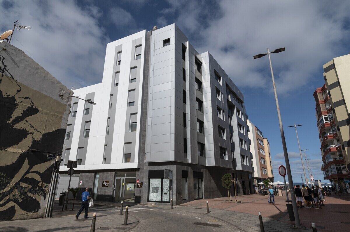 A modern multi-story building with a flat facade, large windows, and a pedestrian area in front.