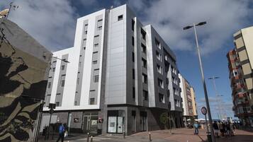 A modern multi-story building with a flat facade, large windows, and a pedestrian area in front.