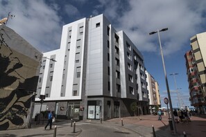 A modern multi-story building with a flat facade, large windows, and a pedestrian area in front. - GuestReady - 02B Livian Suites Int 4 Pax (Las Palmas de Gran Canaria)