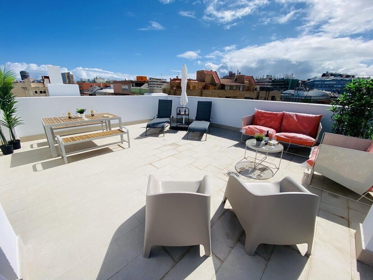 A rooftop terrace with outdoor seating, a table, and a view of the cityscape.