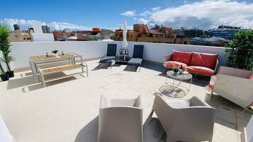 A rooftop terrace with outdoor seating, a table, and a view of the cityscape.