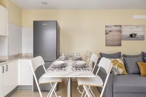 Une cuisine moderne dotée d’un réfrigérateur encastré, d’une table à manger pour quatre personnes et d’un canapé gris agrémenté de coussins.