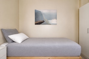 Un lit simple avec un matelas et des oreillers gris, une tête de lit en bois et un tableau représentant un paysage montagneux accroché au mur.