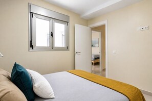 A bedroom with a bed, a window, a door, and a bedside lamp. - GuestReady - 03C Livian Suites Ext 4 Pax (Las Palmas de Gran Canaria)
