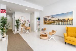 Un espace d’attente moderne agrémenté d’un tableau représentant un paysage urbain, d’un comptoir d’accueil, de sièges et de plantes en pot.