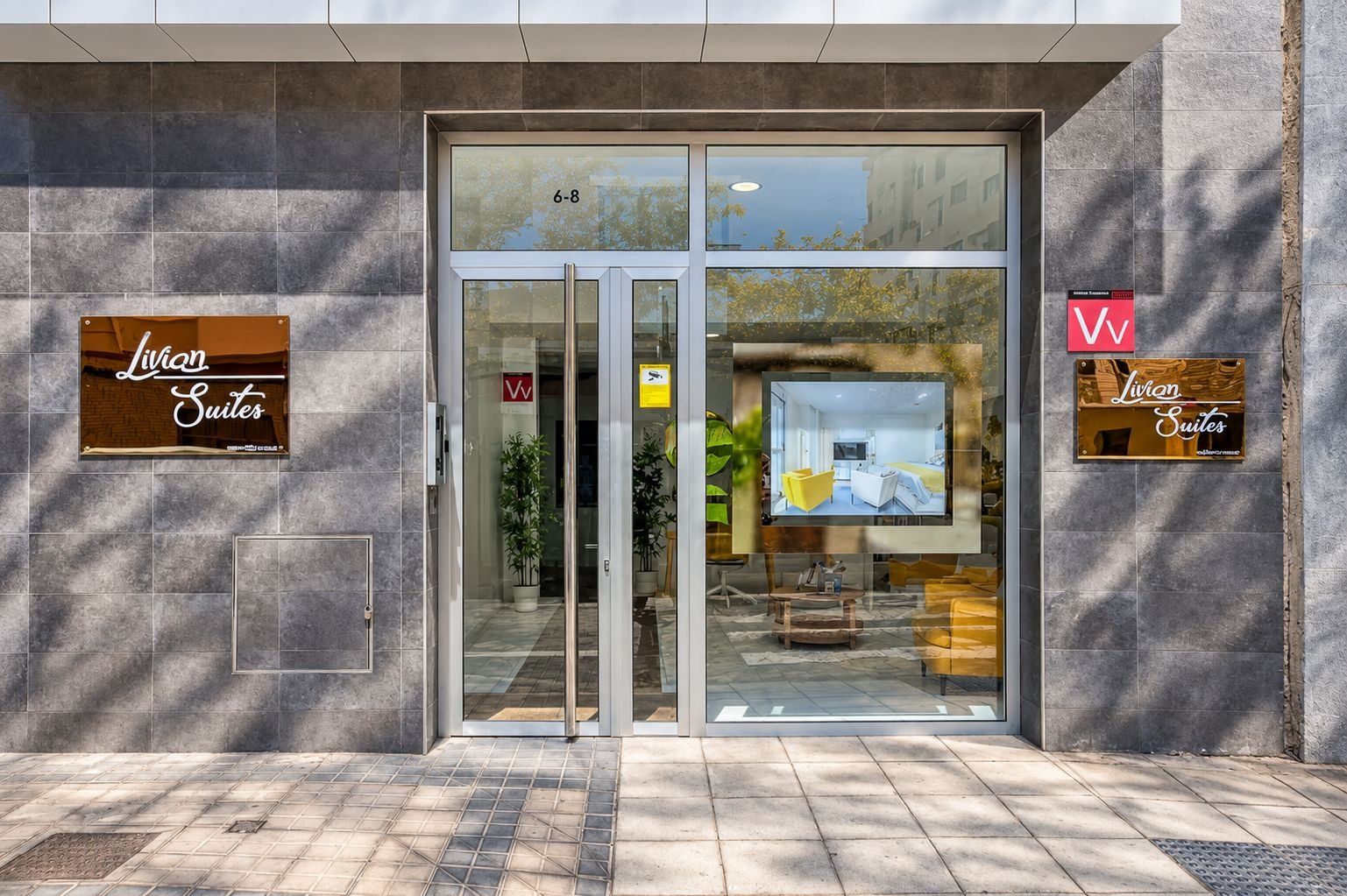 Ein Hotel Eingang mit Glastüren, einem Schild für 'Livan Suites' und einer digitalen Anzeige, die ein Zimmer zeigt.
