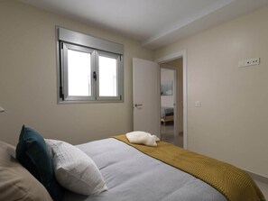 A bedroom with a bed, pillows, a window, and a door leading to another room. - GuestReady - 02C Livian Suites Ext 4 Pax (Las Palmas de Gran Canaria)