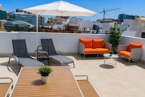 Eine Dachterrasse mit Liegestühlen, einer Sitzecke und einem Tisch mit Blick auf eine Stadtlandschaft.