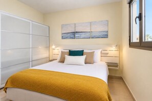 Quarto de hotel com cama, janela, quadro e guarda-roupa.