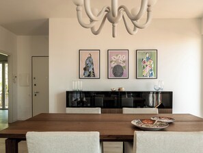 Un coin repas avec une table en bois, quatre chaises, un lustre et trois œuvres d’art encadrées accrochées au mur.