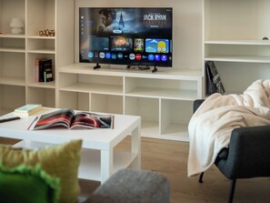 Un salon moderne avec un téléviseur à écran plat, une table basse, une bibliothèque et un fauteuil confortable.