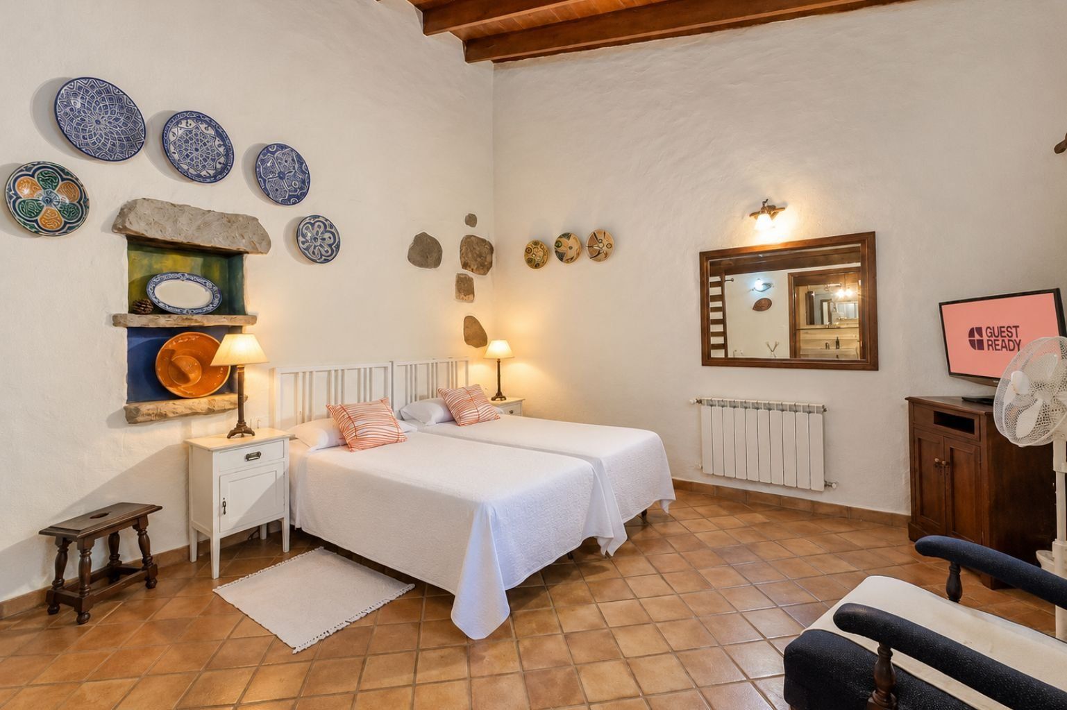 Ein Schlafzimmer mit einem Bett, Nachttischen, einem Spiegel, einem Heizkörper und dekorativen Tellern an der Wand.