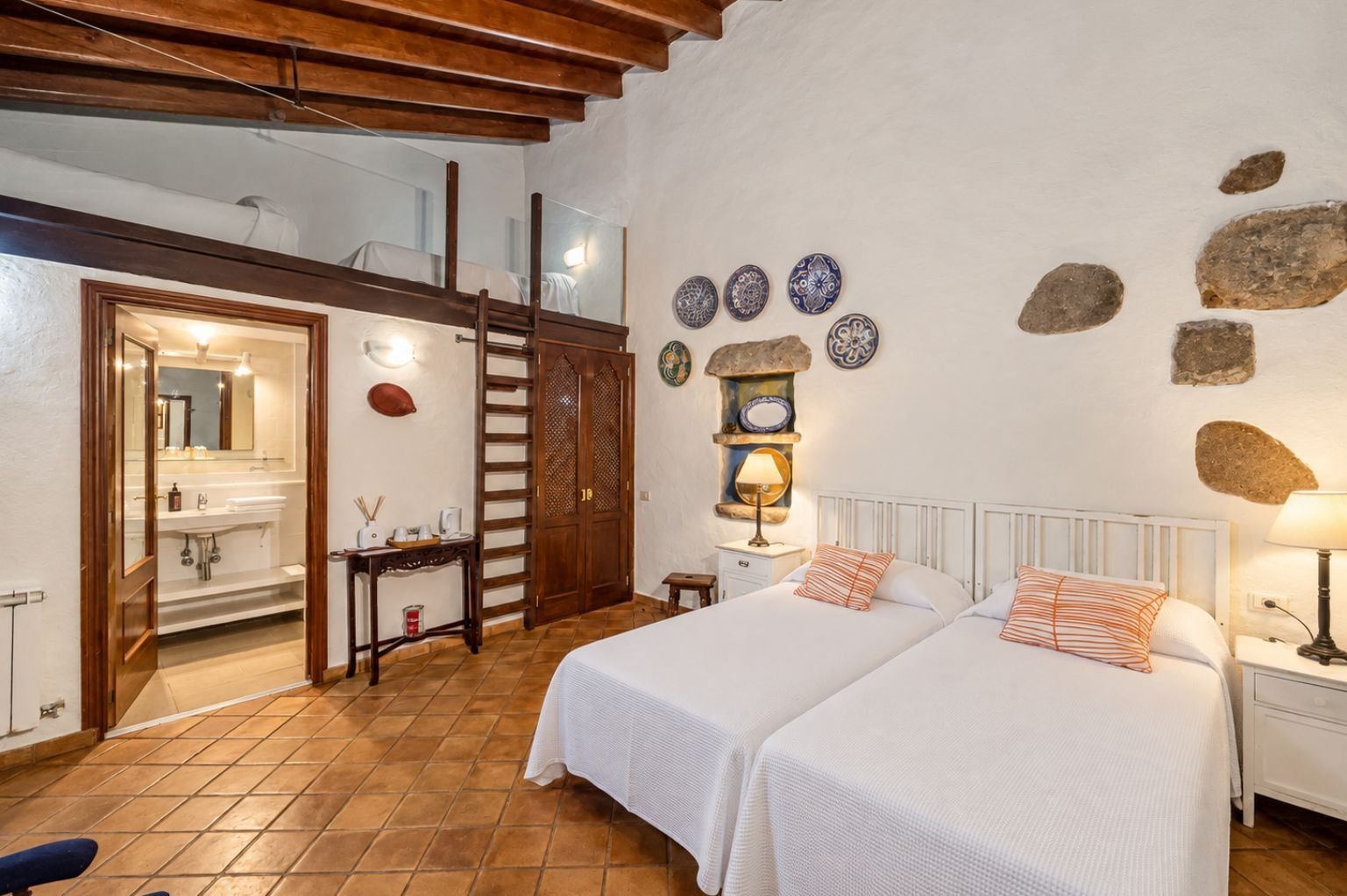 A bedroom with two beds, a bathroom, and a loft area.