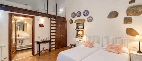 Dormitorio con dos camas, baño y un altillo.