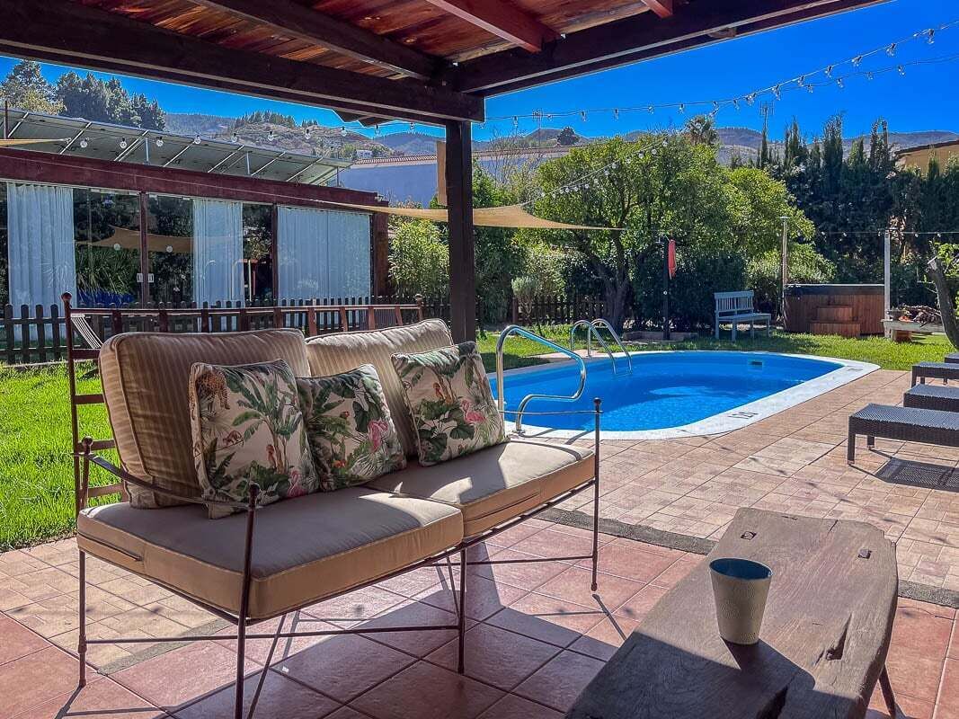 A covered patio with a pool, outdoor furniture, and a view of the surrounding landscape.