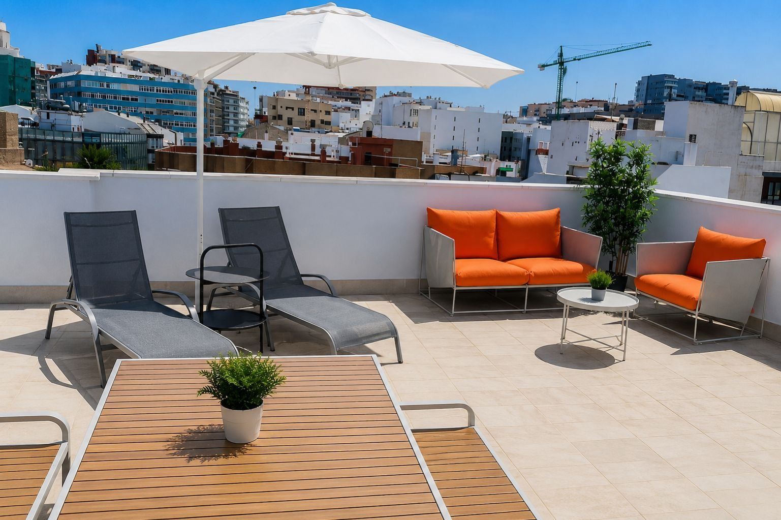 Eine Dachterrasse mit Liegestühlen, einer Sitzecke und einem Tisch mit Blick auf eine Stadtlandschaft.