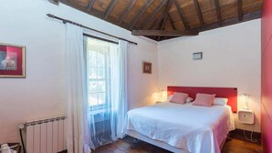 A bedroom with a wooden ceiling, a bed with white bedding, a window with sheer curtains, and a bedside table with a lamp. - GuestReady - Las Calas 8 Double Room Gerbera (Las Palmas de Gran Canaria)