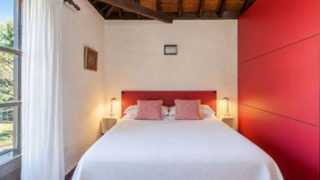 Een hotelkamer met een groot bed, twee bedlampen, een raam met gordijnen en een rode accentmuur.
