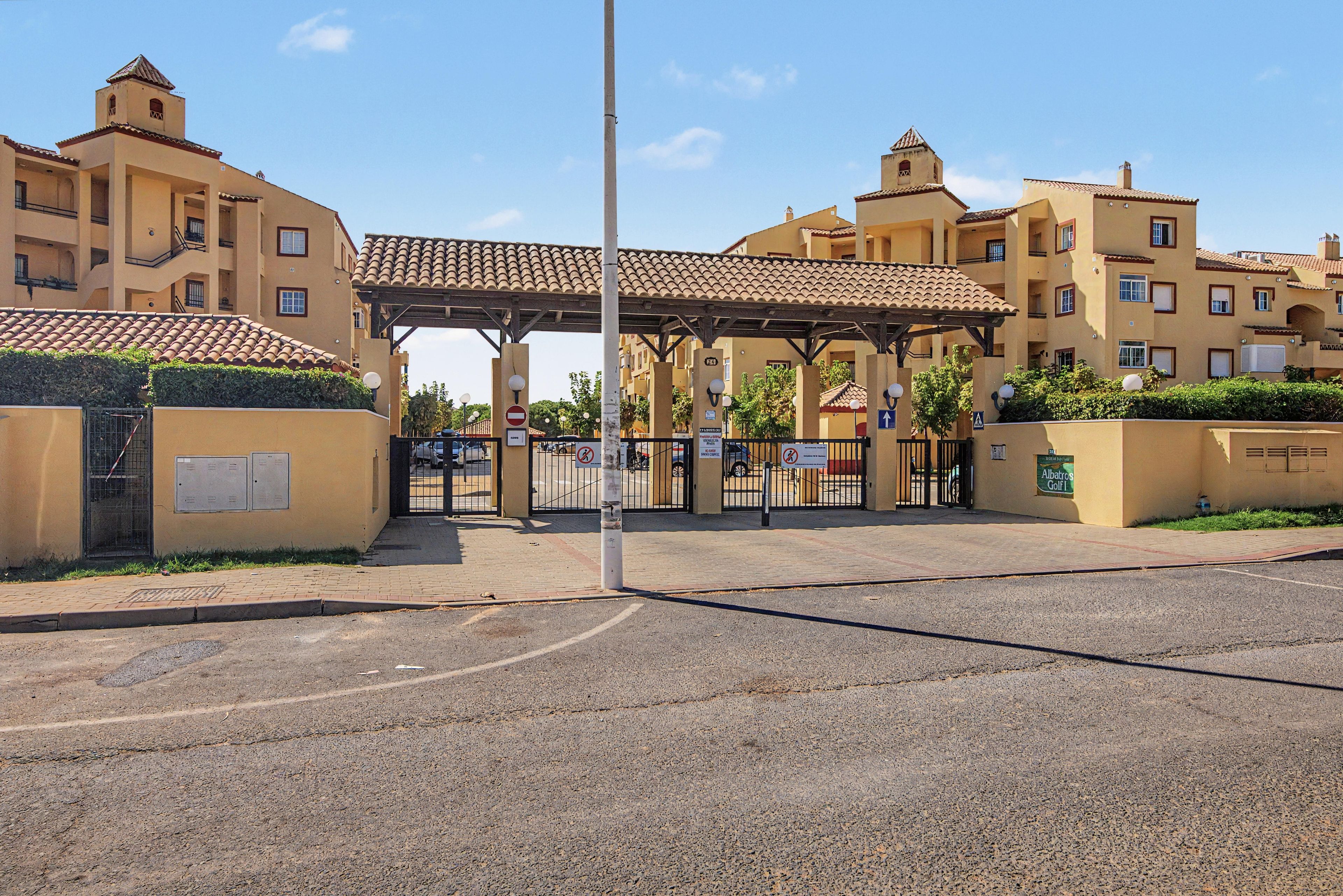 A gated entrance with a covered walkway leading to a building with multiple balconies and a tiled roof.