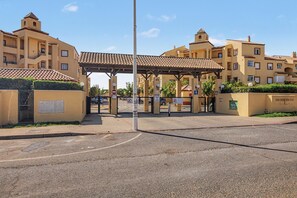 Uma entrada com portão e um corredor coberto que leva a um edifício com várias varandas e um telhado em telhas.