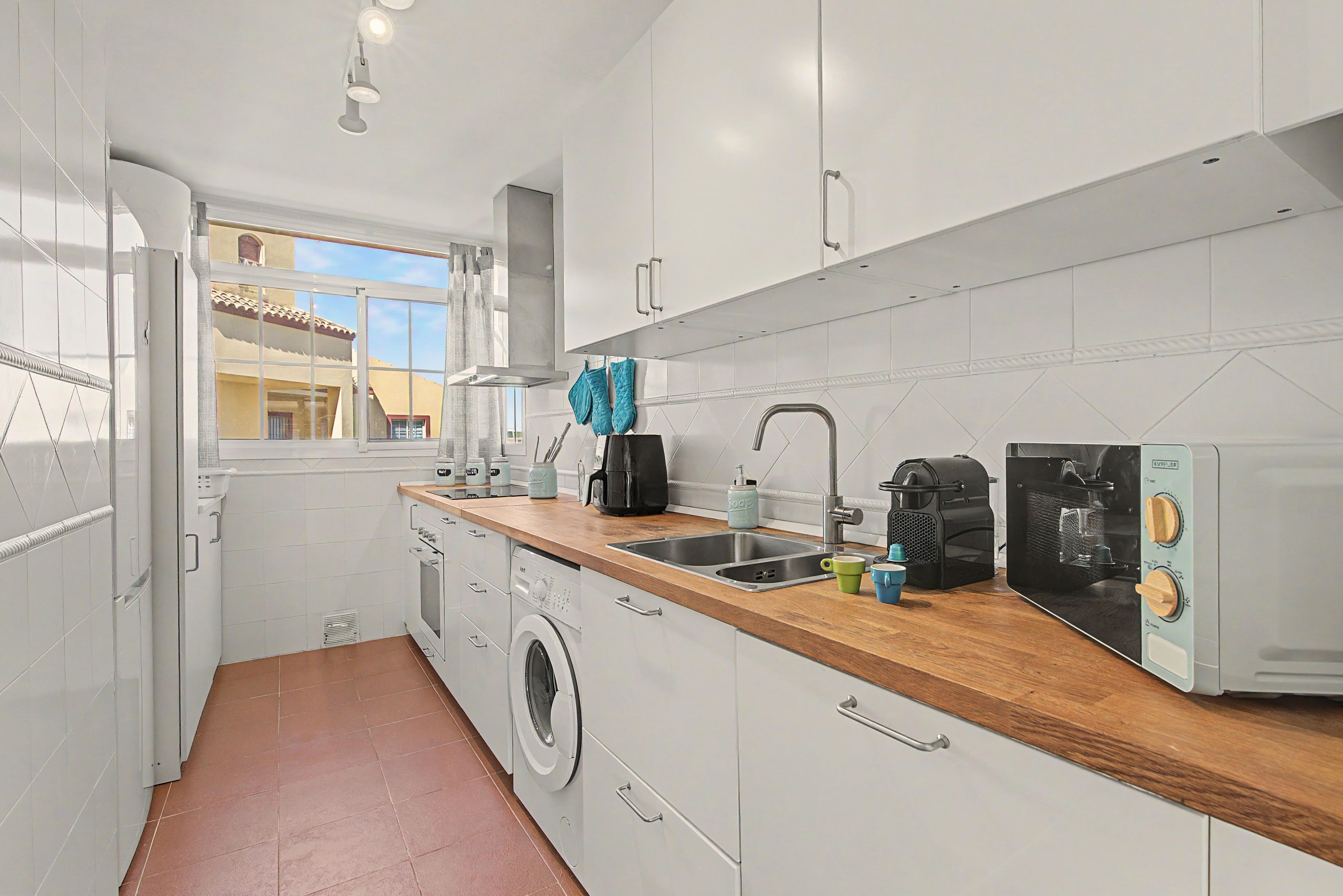A compact kitchen with a washing machine, a coffee maker, and a toaster.