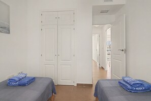 A hotel room with two beds, a door leading to a corridor, and a view into another room.