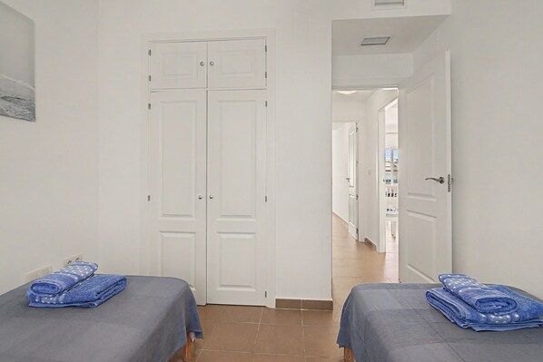 Une chambre d’hôtel avec deux lits, une porte donnant sur un couloir et une vue sur une autre chambre.