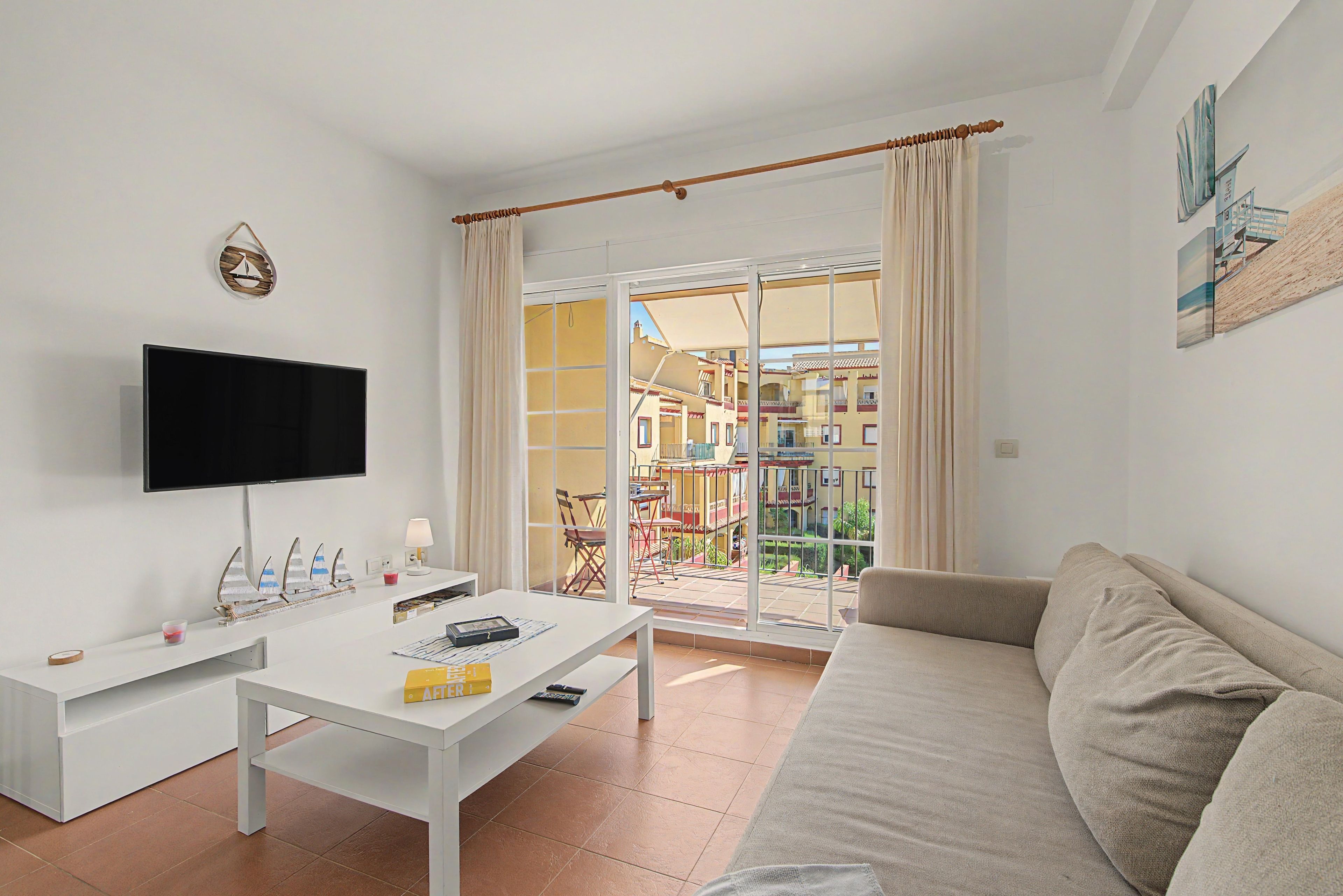 Una sala de estar moderna con un televisor de pantalla plana, una mesa de centro blanca y un sofá color beige.
