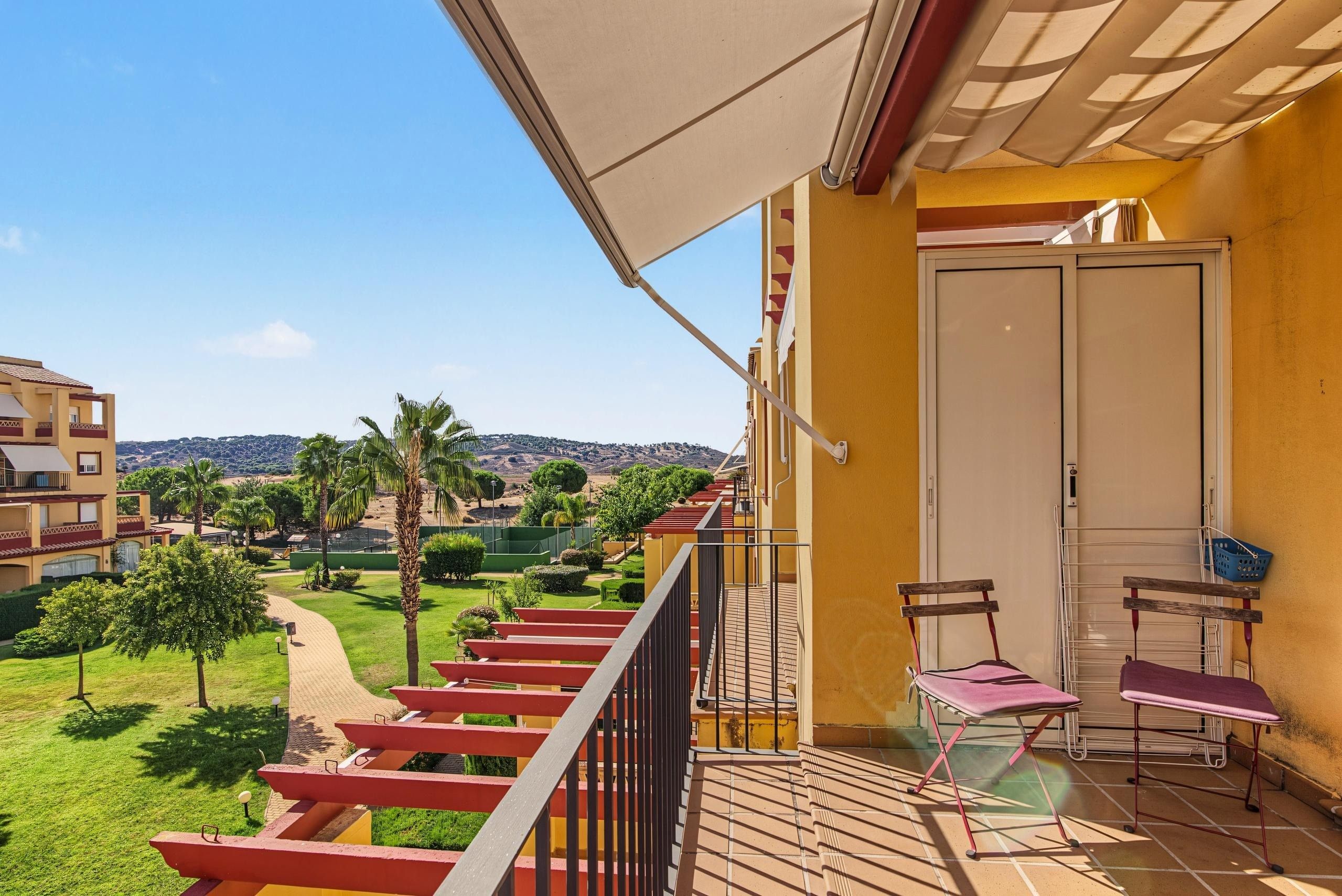 Un balcon donnant sur un jardin aménagé et sur des collines lointaines.