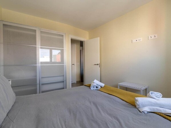 Quarto com cama, guarda-roupa, um banco e porta que dá para outro cômodo.