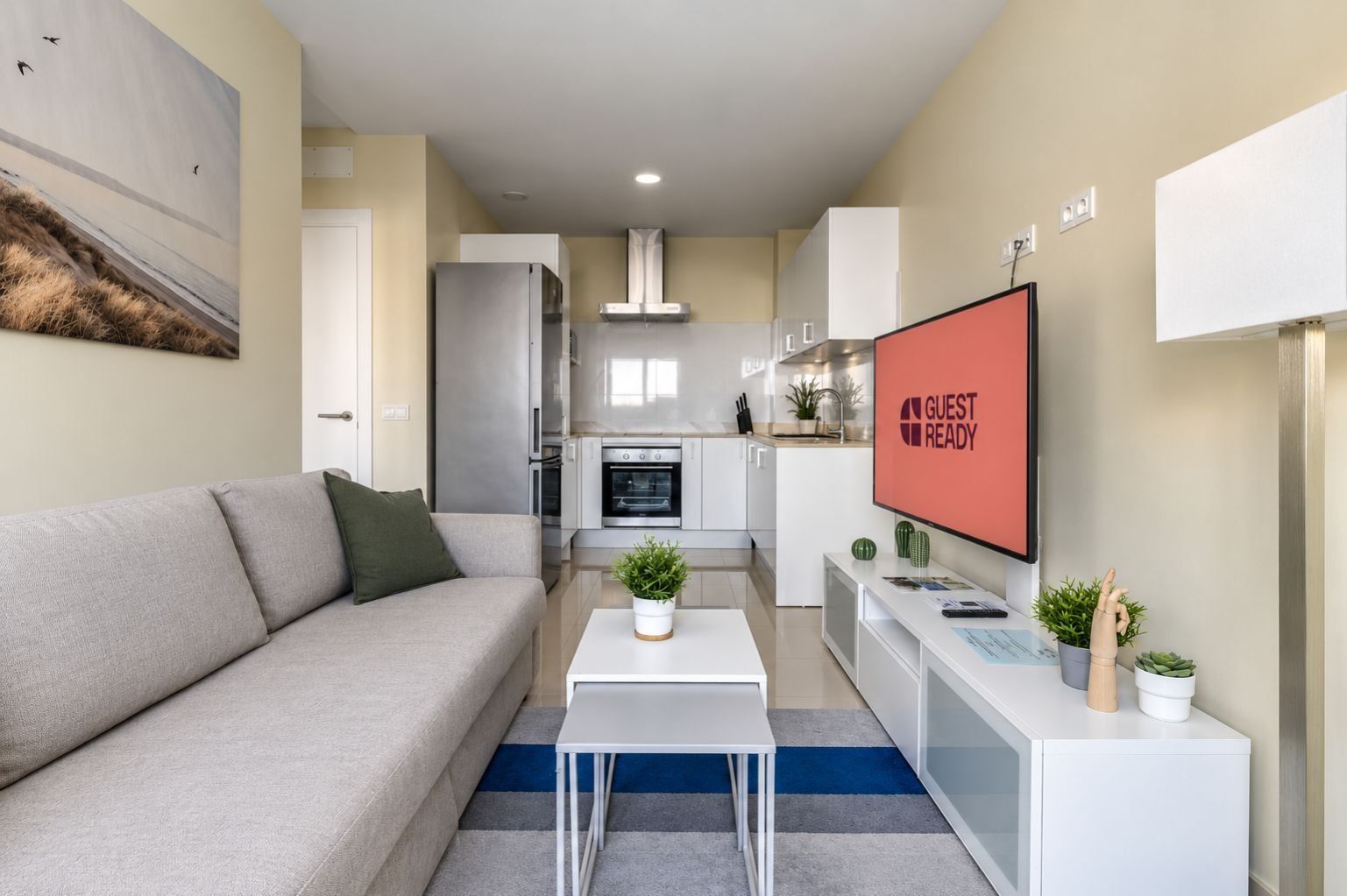 Ein modernes Wohnzimmer mit einer Couch, einem Couchtisch und einem Fernseher, der 'GUEST READY' anzeigt.